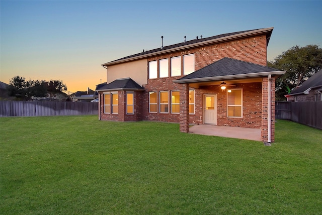 back house at dusk featuring a lawn, a patio area, and ceiling fan