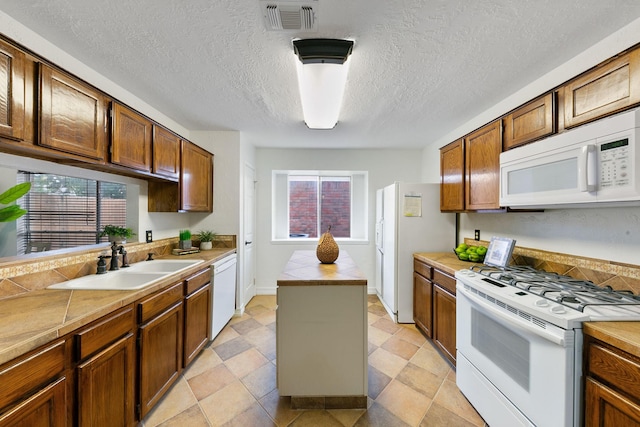 kitchen with a textured ceiling, plenty of natural light, white appliances, and sink