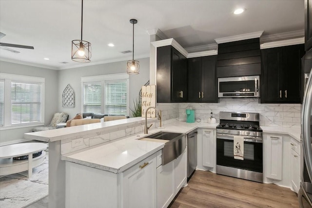 kitchen with kitchen peninsula, light wood-type flooring, stainless steel appliances, sink, and hanging light fixtures