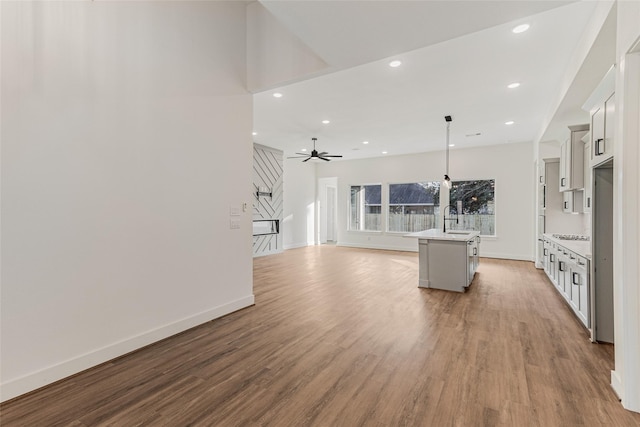 kitchen with ceiling fan, pendant lighting, a kitchen island with sink, white cabinets, and light wood-type flooring