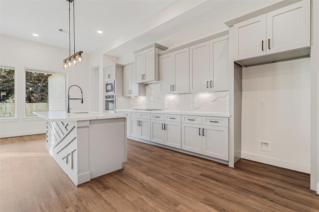 kitchen featuring a center island with sink, white cabinets, dark hardwood / wood-style floors, and decorative light fixtures