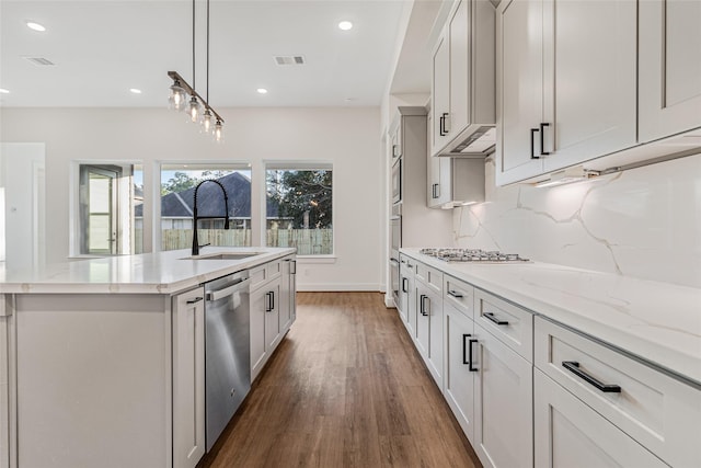 kitchen with dark hardwood / wood-style flooring, pendant lighting, a kitchen island with sink, white cabinets, and appliances with stainless steel finishes