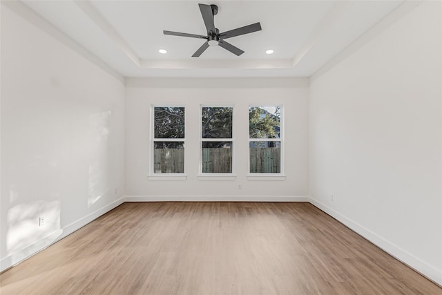 spare room with ceiling fan, light hardwood / wood-style floors, and a raised ceiling