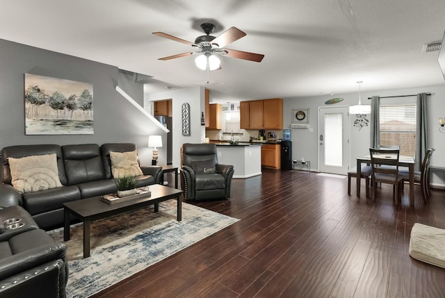 living room featuring a ceiling fan, dark wood-style floors, visible vents, and baseboards