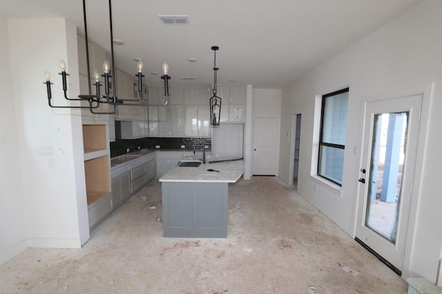 kitchen with gray cabinetry, sink, decorative backsplash, an island with sink, and decorative light fixtures