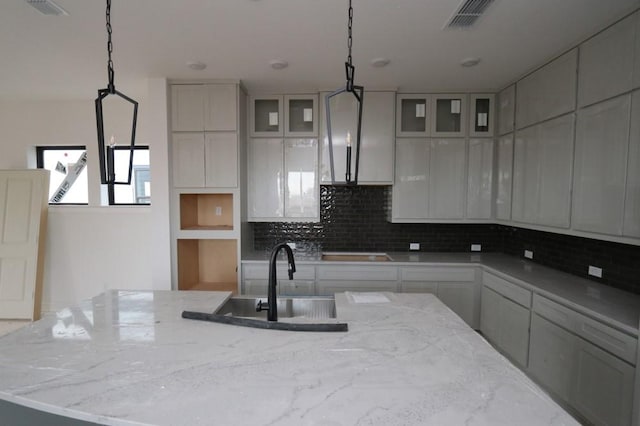 kitchen featuring pendant lighting, a center island, backsplash, sink, and light stone countertops