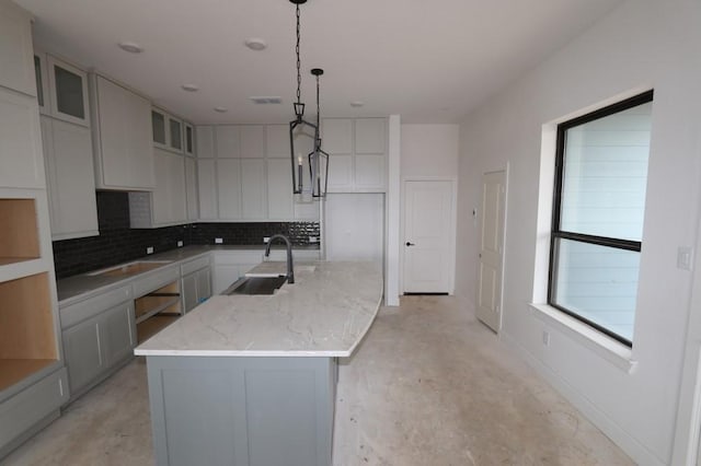 kitchen featuring a center island with sink, tasteful backsplash, light stone counters, pendant lighting, and sink