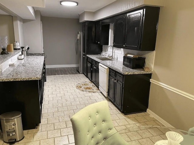 kitchen featuring dishwasher, stainless steel fridge, light stone countertops, and sink