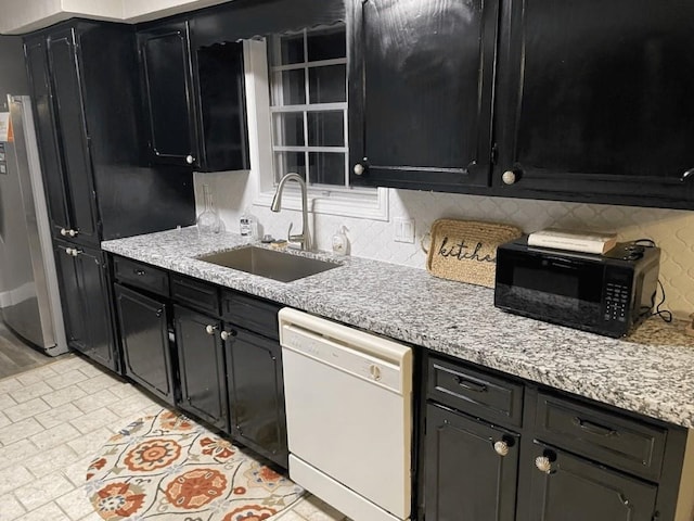 kitchen with backsplash, white dishwasher, sink, light stone counters, and stainless steel refrigerator