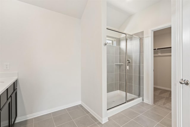 full bathroom featuring a shower stall, vaulted ceiling, a walk in closet, and tile patterned flooring