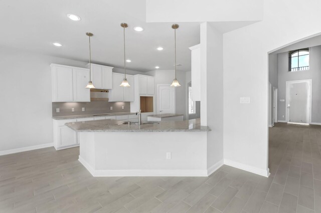 kitchen with pendant lighting, white cabinets, sink, light stone countertops, and kitchen peninsula