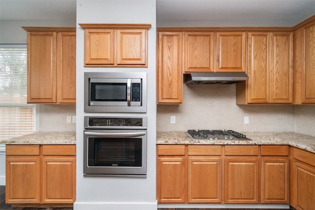 kitchen with tasteful backsplash, appliances with stainless steel finishes, and light stone countertops