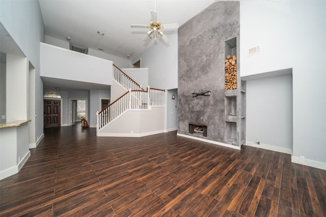 unfurnished living room featuring dark hardwood / wood-style floors, a towering ceiling, a premium fireplace, and ceiling fan