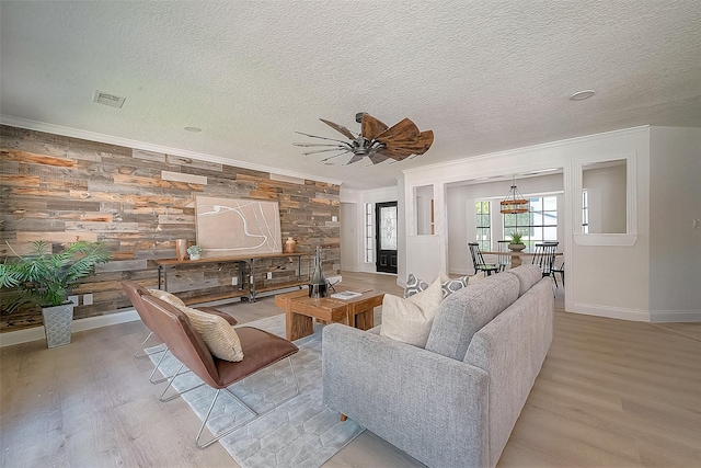 living room with wood walls, ceiling fan, light hardwood / wood-style floors, and a textured ceiling