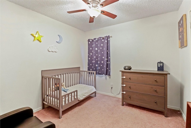 bedroom with ceiling fan, a nursery area, a textured ceiling, and light carpet