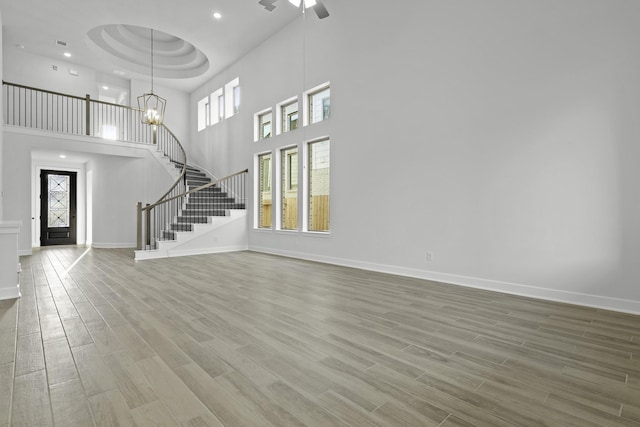 interior space featuring a raised ceiling, hardwood / wood-style floors, a towering ceiling, and ceiling fan with notable chandelier