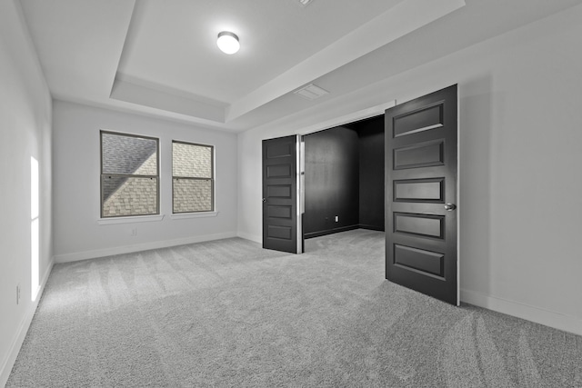 unfurnished bedroom with light colored carpet and a tray ceiling