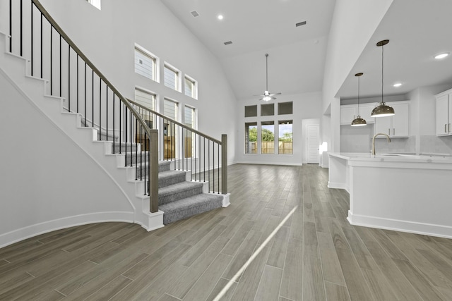 staircase featuring ceiling fan, sink, high vaulted ceiling, and hardwood / wood-style flooring