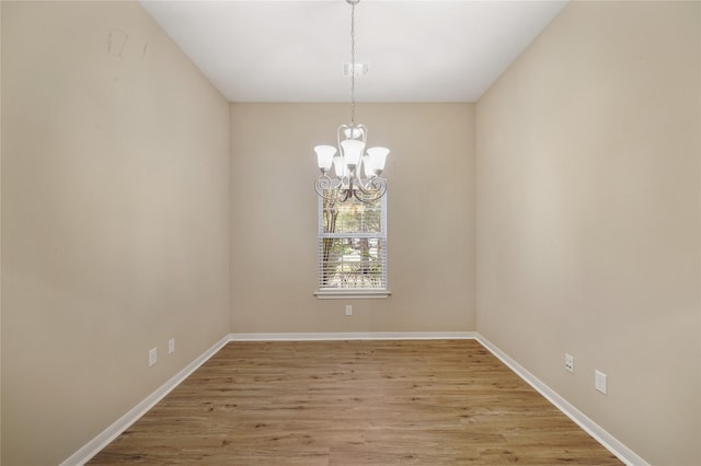 empty room featuring wood-type flooring and an inviting chandelier