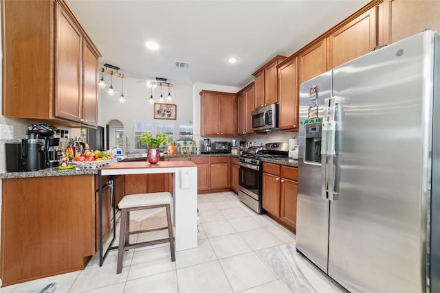 kitchen with dark stone counters, light tile patterned floors, a kitchen bar, kitchen peninsula, and stainless steel appliances