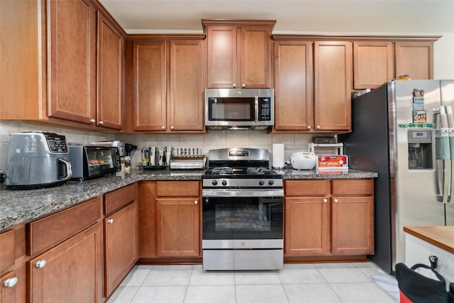 kitchen featuring tasteful backsplash, dark stone countertops, light tile patterned floors, and stainless steel appliances