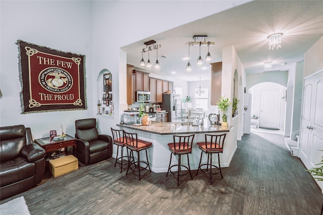 kitchen featuring kitchen peninsula, a kitchen breakfast bar, stainless steel appliances, dark wood-type flooring, and pendant lighting