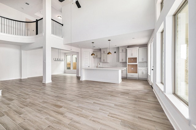 unfurnished living room featuring a high ceiling, light hardwood / wood-style flooring, ceiling fan, and sink