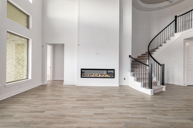 unfurnished living room featuring a high ceiling and light hardwood / wood-style flooring