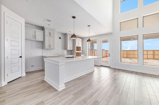 kitchen with decorative backsplash, light wood-type flooring, sink, hanging light fixtures, and an island with sink