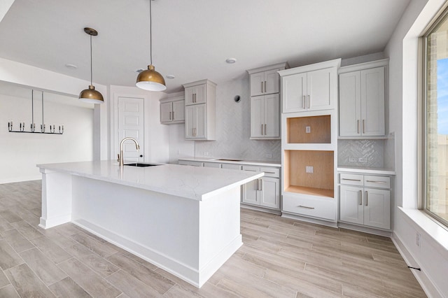 kitchen featuring a wealth of natural light, a kitchen island with sink, hanging light fixtures, and sink