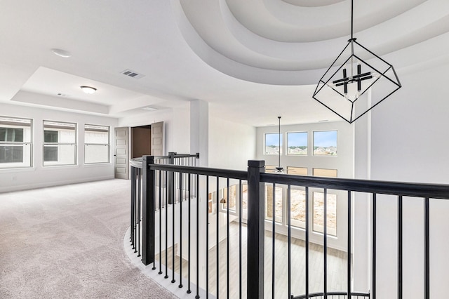 hall featuring a raised ceiling, a wealth of natural light, light colored carpet, and an inviting chandelier