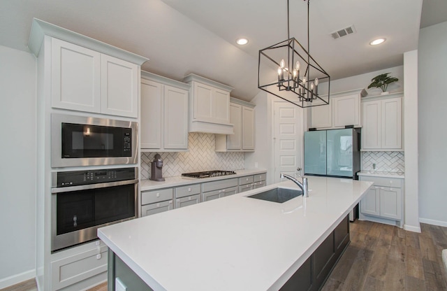 kitchen featuring sink, stainless steel appliances, dark hardwood / wood-style floors, and a center island with sink