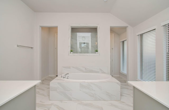 bathroom featuring vanity, vaulted ceiling, and tiled tub