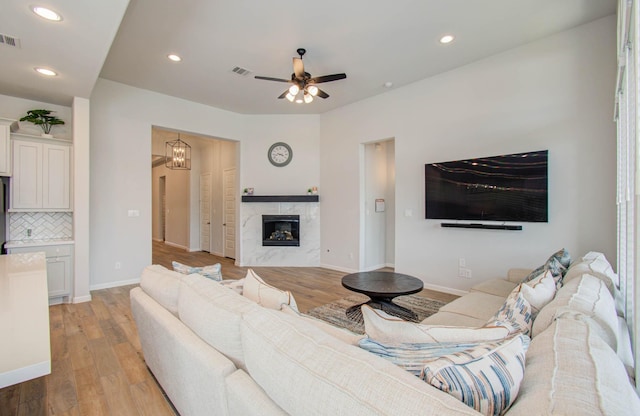 living room with ceiling fan with notable chandelier, light hardwood / wood-style floors, and a fireplace