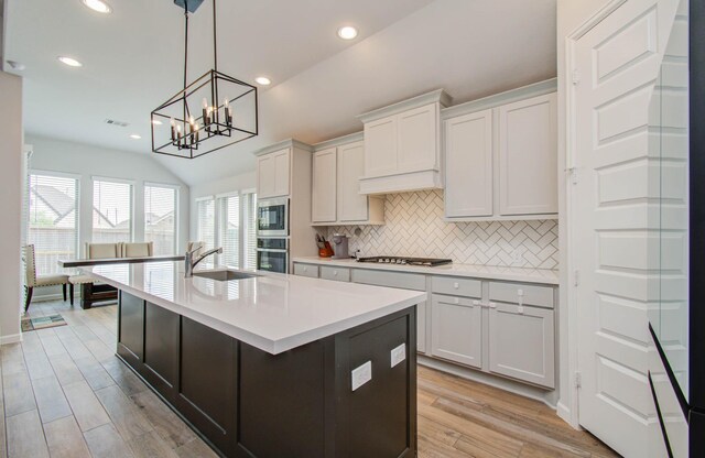 kitchen featuring light wood-type flooring, stainless steel appliances, vaulted ceiling, white cabinets, and hanging light fixtures