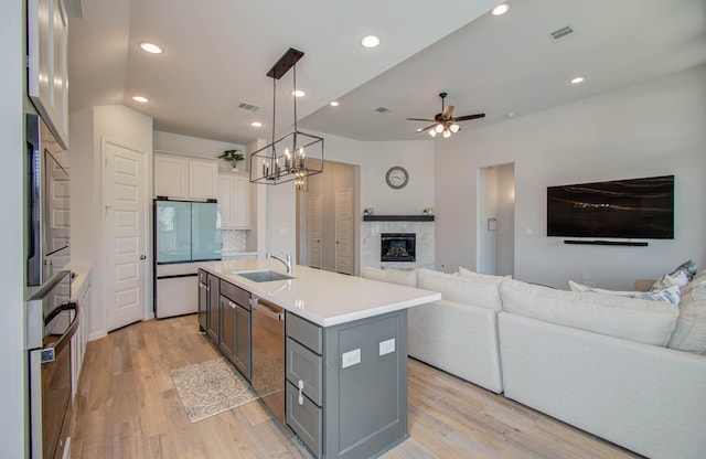 kitchen with light wood-type flooring, an island with sink, appliances with stainless steel finishes, decorative light fixtures, and white cabinetry