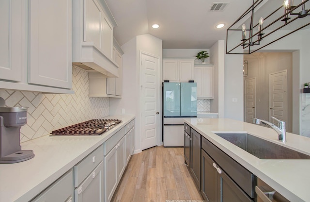 kitchen featuring stainless steel gas stovetop, sink, hanging light fixtures, light hardwood / wood-style floors, and white fridge