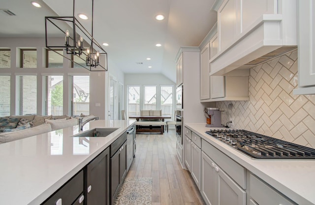 kitchen with sink, stainless steel appliances, backsplash, light hardwood / wood-style floors, and decorative light fixtures