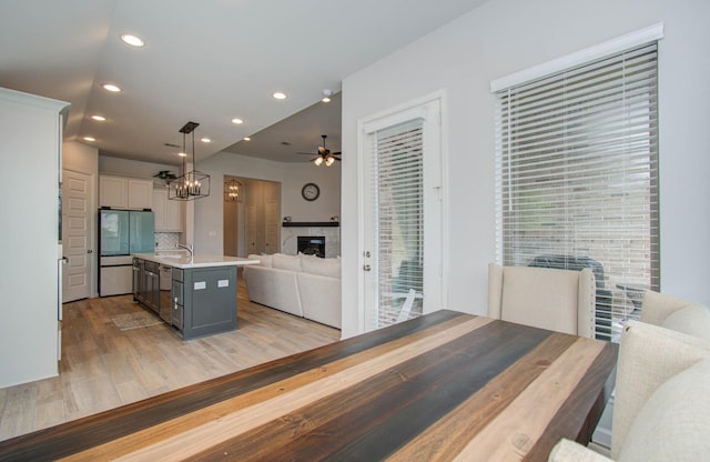 kitchen featuring light hardwood / wood-style floors, pendant lighting, white fridge, white cabinetry, and an island with sink