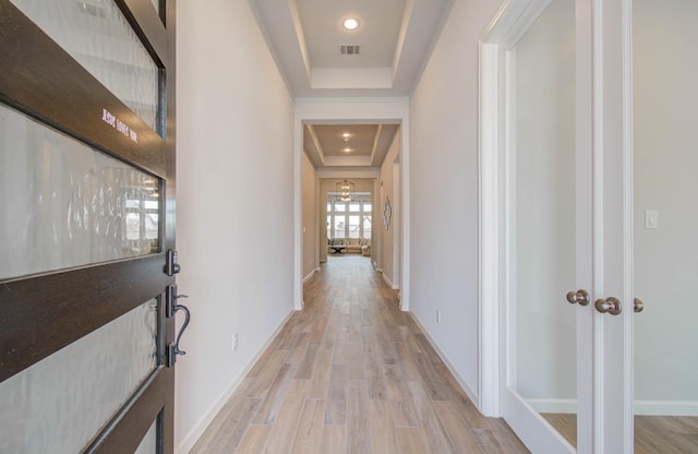 corridor with a raised ceiling and light hardwood / wood-style floors