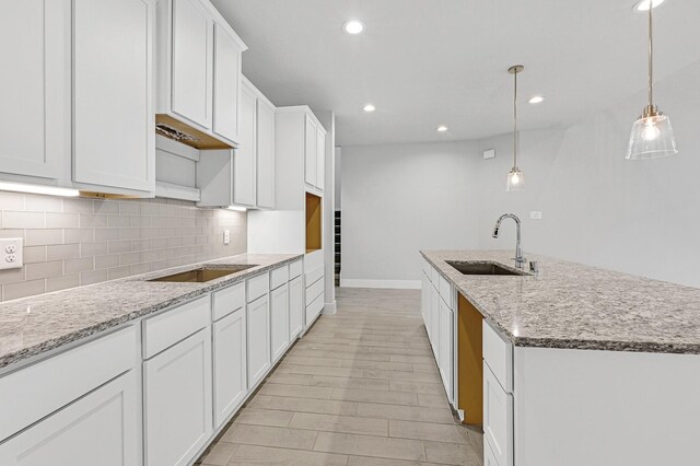 kitchen featuring white cabinetry, sink, hanging light fixtures, light stone counters, and an island with sink