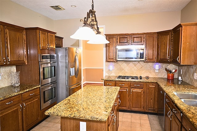 kitchen with light stone counters, hanging light fixtures, a center island, and appliances with stainless steel finishes