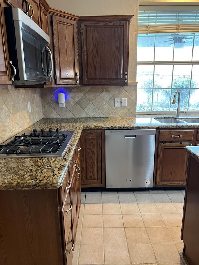 kitchen with sink, backsplash, stainless steel appliances, dark brown cabinetry, and light stone countertops