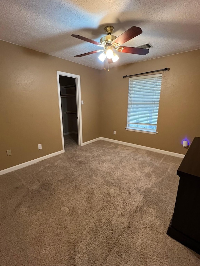 unfurnished bedroom featuring ceiling fan, a spacious closet, a textured ceiling, and carpet