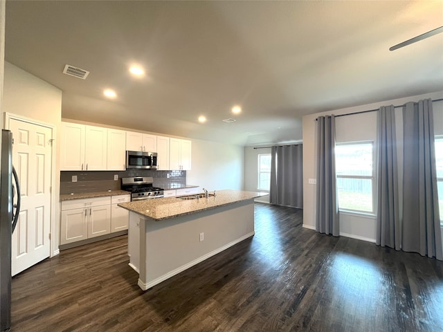 kitchen featuring decorative backsplash, appliances with stainless steel finishes, a kitchen island with sink, dark hardwood / wood-style floors, and white cabinetry