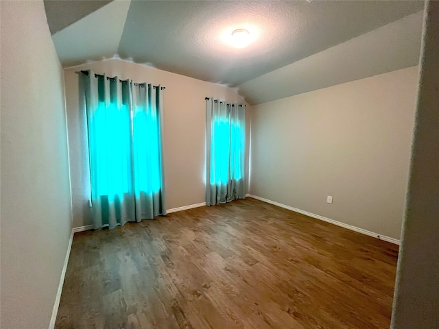 spare room featuring wood-type flooring and vaulted ceiling