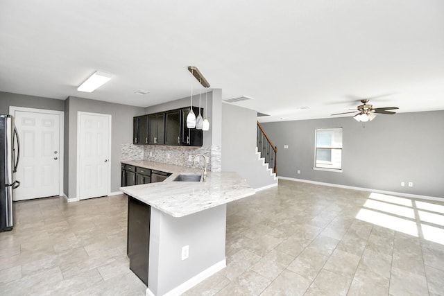 kitchen featuring kitchen peninsula, stainless steel fridge, backsplash, sink, and hanging light fixtures