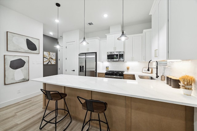 kitchen with kitchen peninsula, stainless steel appliances, sink, decorative light fixtures, and white cabinetry