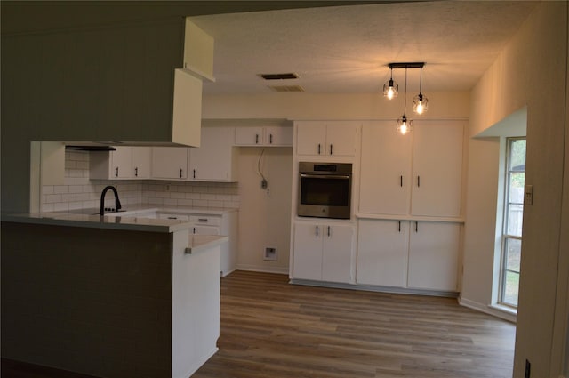 kitchen with stainless steel oven, white cabinets, hanging light fixtures, light hardwood / wood-style flooring, and kitchen peninsula