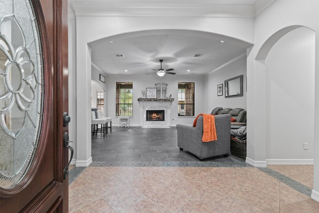 tiled foyer with ceiling fan and crown molding